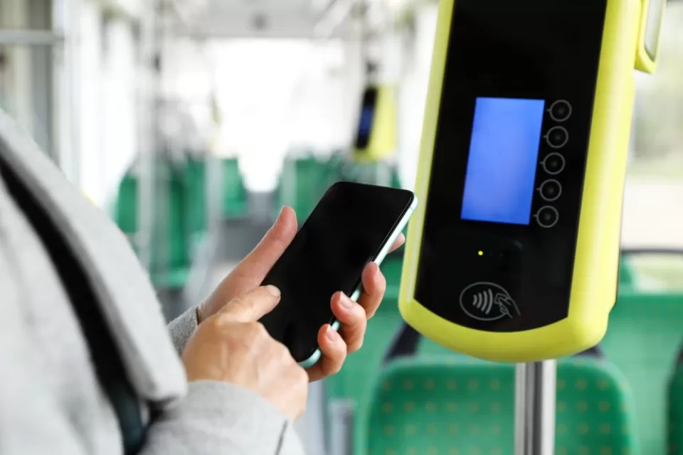 Close-up of person holding up smartphone next to contactless fare reading device on bus